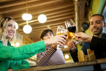 From below happy diverse male and female friend clinking glasses of alcohol during party in weekend in pub. Man and women proposing toast during party