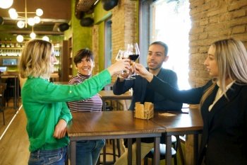 Happy diverse group of friends clinking glasses of alcohol during party in weekend in pub. Man and women proposing toast during party