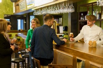 Man ordering beer from barkeeper while standing near happy talking women on weekend day in pub. Clients and bartender in an elegant bar