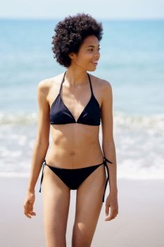 Positive black woman in bikini walking on the beach smiling. Girl with afro hairstyle coming out of the water at the beach.. Positive black woman in bikini walking on the beach smiling.