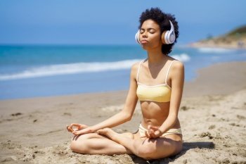 Black female in lotus pose doing mindfulness listening to a meditation with wireless headphones.. Black girl in lotus pose doing mindfulness listening to a meditation with wireless headphones.