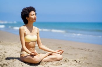 Black woman sitting on the beach doing mindfulness meditation in lotus position. Young female wearing yellow bikini.. Black woman sitting on the beach doing mindfulness meditation in lotus position.