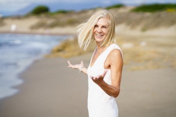 Smiling mature female opening her arms on a tropical beach. Elderly woman enjoying her retirement walking on the beach.. Happy mature woman walking on the beach, spending her leisure time, enjoying her free time