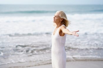 Mature female opening her arms on a tropical beach, spending her leisure time. Elderly woman enjoying her retirement at a seaside retreat.. Mature female opening her arms on the beach, spending her leisure time, enjoying her free time
