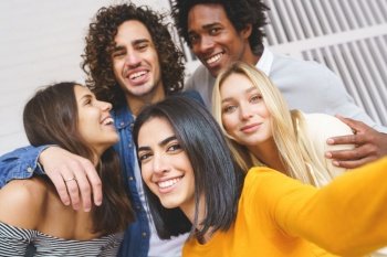 Group of delighted diverse friends embracing and taking self shot while having fun and looking at camera. Company of multiethnic friends taking selfie