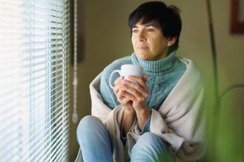 Mid adult woman drinking coffee and looking out of the window in winter day. Female in her 50s. Mid adult woman drinking coffee and looking out of the window in winter day.