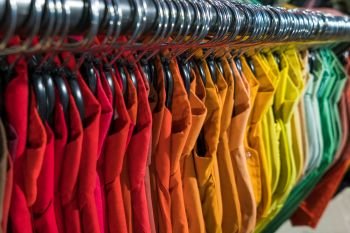 Male men’s shirts sorted in color order on hangers on a thrift shop or wardrobe closet rail