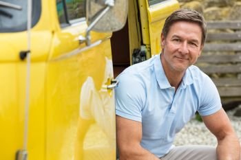 Portrait shot of an attractive, successful and happy middle aged man male wearing a blue polo shirt, sitting in the doorway of a bus, van or truck 