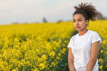 Beautiful mixed race African American girl teenager female young woman sad depressed or thoughtful at the end of a path in a field of yellow flowers
