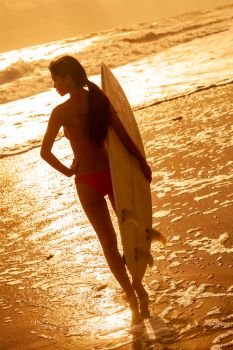 Rear view of beautiful sexy young woman surfer girl in pink bikini with white surfboard on a beach at sunset or sunrise