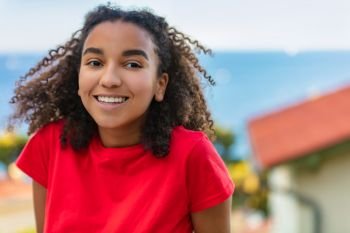 Outdoor portrait of beautiful happy mixed race African American girl teenager female young woman smiling with perfect teeth and the sea coastline behind her