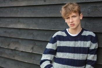 Serious male boy teenager young adult outside leaning on a wall wearing a striped jumper