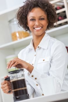 Beautiful happy mixed race African American girl or young woman with perfect teeth in her kitchen, making coffee with a French press or cafetiere