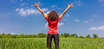 Rear view panoramic web banner of young woman girl female runner jogger standing arms raised  celebrating standing in green field with blue sky