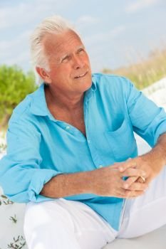 Portrait of a happy attractive handsome senior man sitting down outside on a beach looking thoughtful