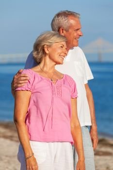 Happy senior man and woman couple standing embracing on vacation on a deserted white sand beach with bright clear blue sky and calm sea