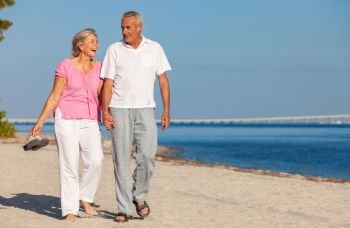 Happy senior man and woman couple walking laughing holding hands on vacation on a deserted tropical beach with bright clear blue sky and calm sea