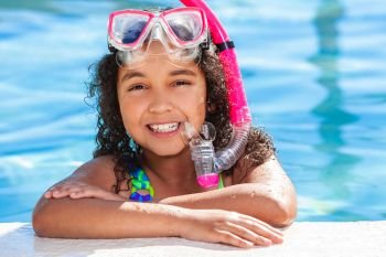 Biracial African American happy young girl child relaxing on the side of a swimming pool wearing pink goggles and snorkel