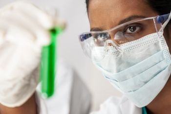 Asian female medical or scientific researcher or doctor looking at a test tube of green solution in a lab or laboratory