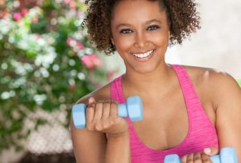 Beautiful young smiling mixed race biracial black African American woman exercising outside using weights, fitness aerobic exercising pilates.