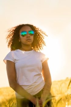 Beautiful mixed race biracial African American female girl teenager young woman wearing sunglassesat sunset or sunrise in a field of wheat, corn or barley
