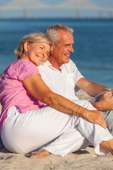 Happy senior man and woman couple sitting, smiling and laughing on a sunny beach 