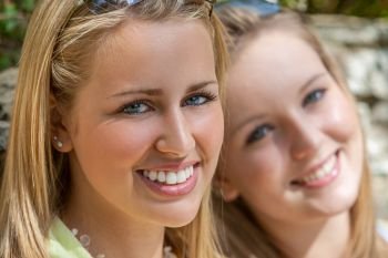 Two happy blonde teenage girls teen female friends outside smiling with perfect teeth
