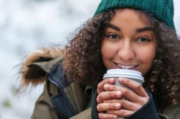 Beautiful happy mixed race African American girl teenager female young woman smiling drinking takeaway coffee outside wearing a green hat and coat