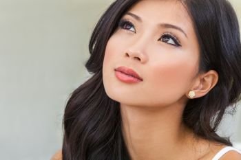 Close up portrait of a beautiful thoughtful Chinese Asian young woman or girl with perfect make up looking up and thinking