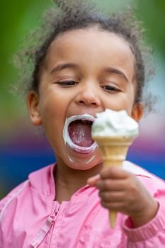 Outdoor portrait of beautiful happy cute, kid, mixed race African American girl female child eating an ice cream cornet with a messy mouth and face