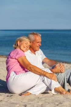 Happy senior man and woman couple sitting together on a deserted tropical beach with bright clear blue sky