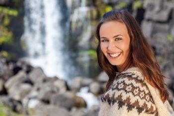 Beautiful Icelandic woman wearing traditionally patterned knitwear smiling in the mountains by a waterfall in Northern Iceland