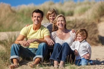 Happy family of mother, father and two sons, sitting laughing and having fun in the sand dunes of a sunny beach