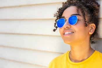 Girl teenager cool teen mixed race biracial African American female young woman wearing blue sunglasses and a yellow t-shirt on vacation smiling in summer sunshine