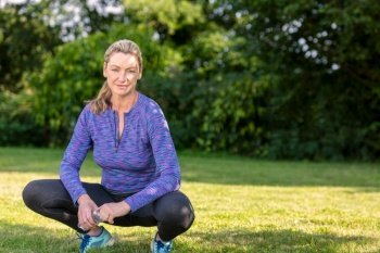 Outdoor portrait of an attractive middle aged blonde woman smiling drinking water relaxing after exercising, running or fitness lifestyle