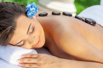 A woman with a flower in her hair relaxing at a health spa while having a hot stone treatment or massage