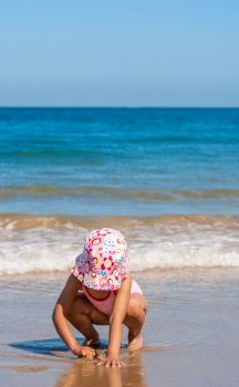 Cute little girl female child sitting playing on a beach on pink swimming costume and hat