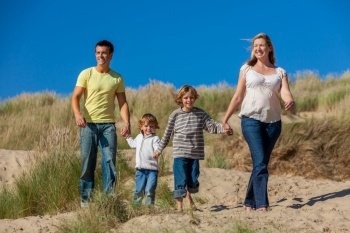 Happy family of mother, father and two sons, man woman children walking holding hands, having fun in the sand dunes of a sunny beach