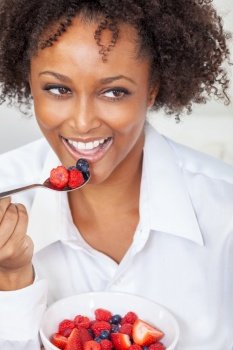 African American biracial girl female young woman with perfect teeth eating a bowl of fresh fruit, strawberries, raspberries and blueberries. Healthy eating and lifestyle concept.