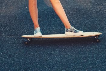 Closeup of skateboarder legs. Woman in sneakers riding skateboard outdoor on asphalt surface. Copyspace on asphalt.. Closeup of skateboarder legs. Woman in sneakers riding skateboard outdoor.