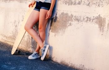 Bare legs of skater girl in short shorts leaning back used wall with her longboard near with her legs crossed a lot of space for text. Bare legs of skater girl in short shorts leaning back used wall with her longboard near with her legs crossed