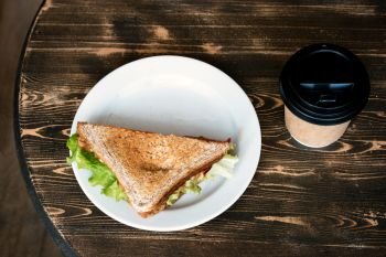 Lunch with triangle sandwich on dark table background top view. Sandwich on plate and takeaway cup near. Lunch with triangle sandwich on dark table background top view