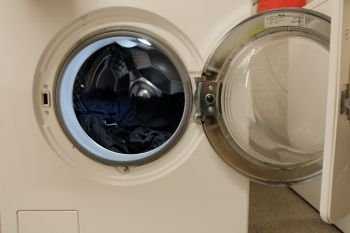 Open washing machine with some clothes inside drum