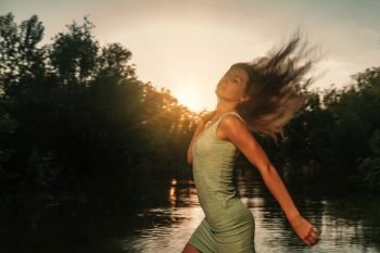Beautiful blonde girl with long hair in short dress running at sunset on the river side with her hair flying in the air. Beautiful blonde girl with long hair in short dress running at sunset on the river side with her hair fly in an air