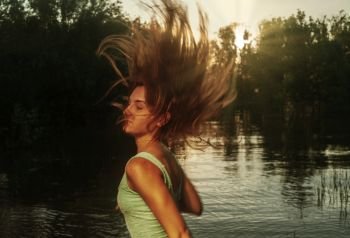 Young woman enjoying freedom feeling happy running at sunset with her hairs flying in the air. Young attractive woman in sunset light. Carefree and happyness concept. Young woman enjoying freedom feeling happy running at sunset with her hairs flying in an air