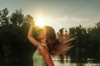 Beautiful young woman running on a riverside at sunset, in front of setting sun, copyspace. Beautiful young woman running on a riverside at sunset