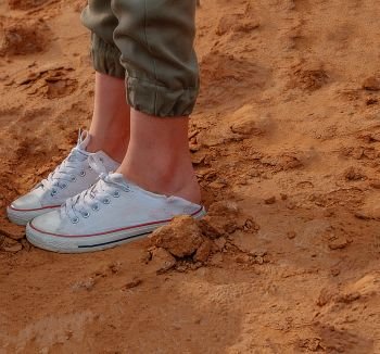Girls legs in trainers on bare dirt, shot with copyspace. Girls legs in trainers on bare dirt