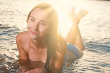 Happy Girl lying in sea waves and looking away in sunset light from back. Cute Girl lying in sea waves and looking away in sunset light from back