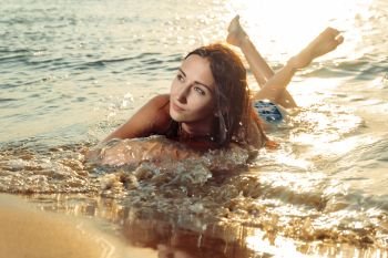 Girl lying in sea waves and looking away in sunset light from back