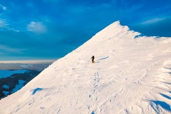 Mountaineer with dog climbing on a slope at snowy mountain top in sunset evening